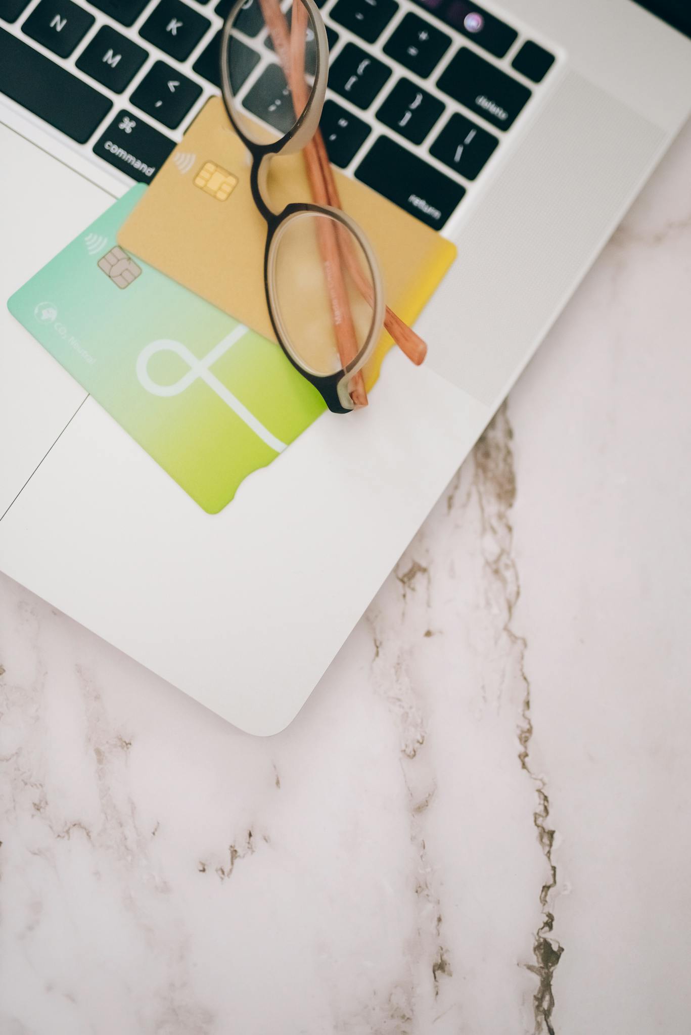 Eyeglasses and credit cards placed on a laptop keyboard for online work.